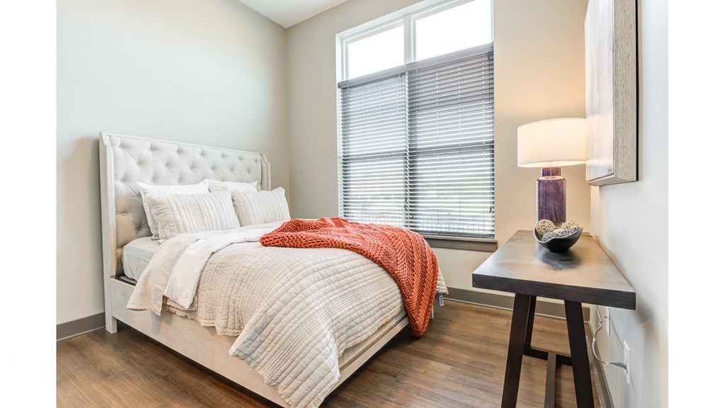 A bedroom with a bed, a side table with a lamp, and a window with blinds.