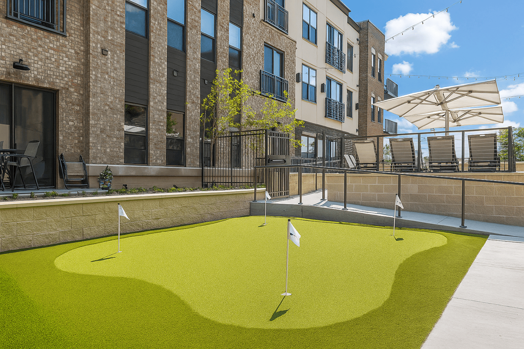 A small putting green is surrounded by a brick building.