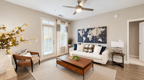 Model apartment living room with a white sofa, wood coffee table and balcony door at Argento at Riverwatch Apartments in Augusta, GA.