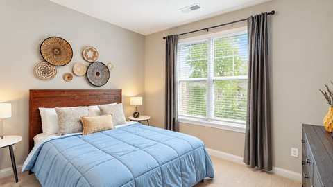 Model apartment bedroom with blue bedding, a wood headboard and a large window at Argento at Riverwatch Apartments in Augusta, GA.