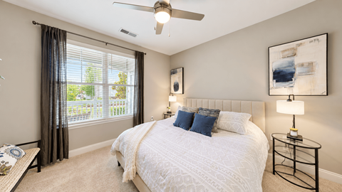 Model apartment bedroom with an upholstered headboard, white bedding and navy pillows at Argento at Riverwatch Apartments in Augusta, GA.