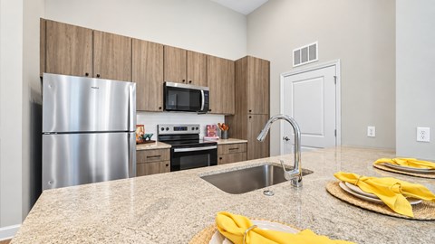 Apartment kitchen with stainless steel appliances, wood-look cabinets and a breakfast bar with an undermount sink.