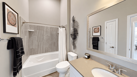 A2 apartment bathroom with a tiled tub surround, white vanity, and framed mirror at Argento at the Bridges in McDonough, GA.