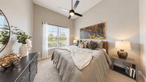 Furnished A2 apartment bedroom with layered bedding, bedside lamps, and a dresser at Argento at the Bridges in McDonough, GA.
