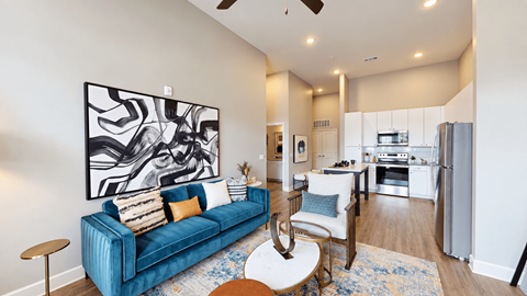 A2 apartment living room with a blue sofa, accent chair, and open kitchen at Argento at the Bridges in McDonough, GA.