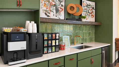 A kitchen with green cabinets and a black coffee maker.
