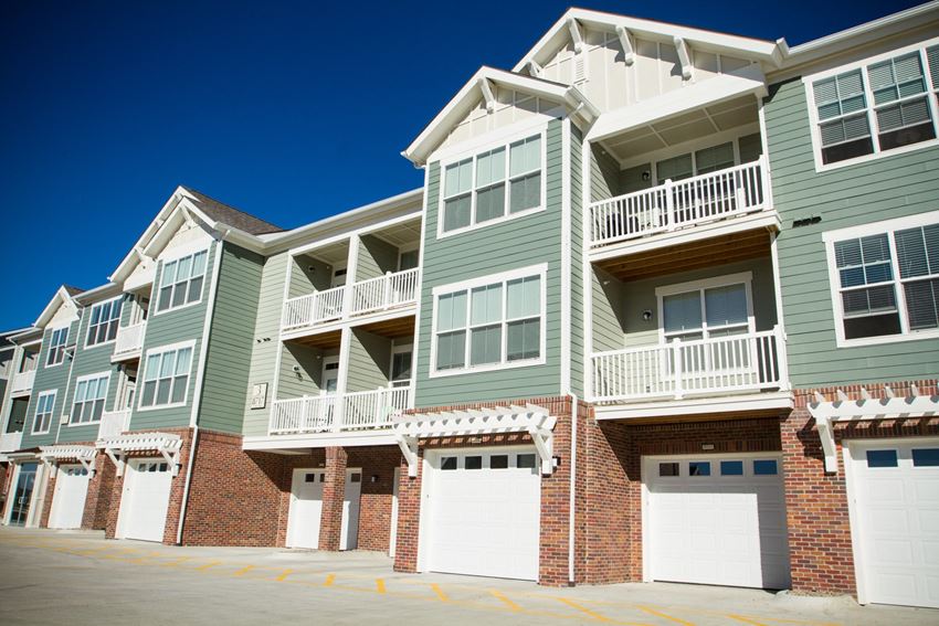 Exterior of building, tall green and brick building, white garage doors and patios