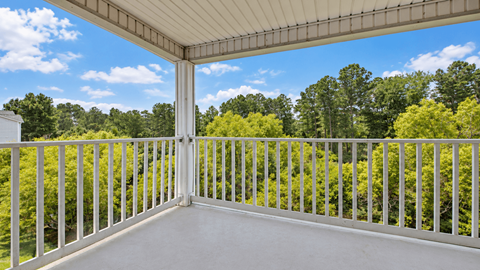 A white balcony with a metal railing overlooking a forest.