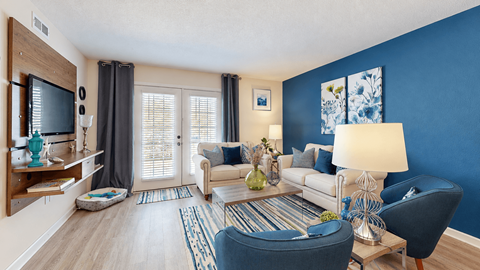 Furnished living room with a blue accent wall, cream seating and French doors at Canterbury Apartments in Myrtle Beach, SC.