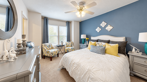 Furnished bedroom with a white upholstered headboard, blue accent wall and window seating at Canterbury Apartments in Myrtle Beach, SC.