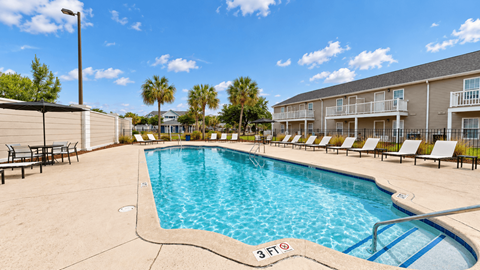 Outdoor swimming pool with entry steps, lounge chairs and palm trees at Canterbury Apartments in Myrtle Beach, SC.