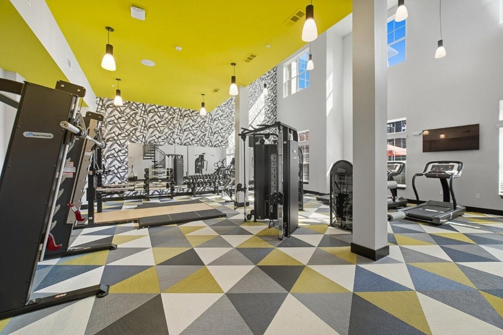 A gym with a variety of equipment and a geometric patterned floor.