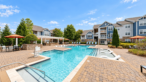 Outdoor swimming pool surrounded by a paved deck, lounge chairs, and umbrellas at Enclave at Bailes Ridge in Indian Land, SC.