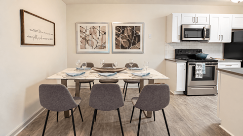 Dining table with six chairs beside a kitchen with white cabinets at Icon Avondale Apartments in Decatur, GA.
