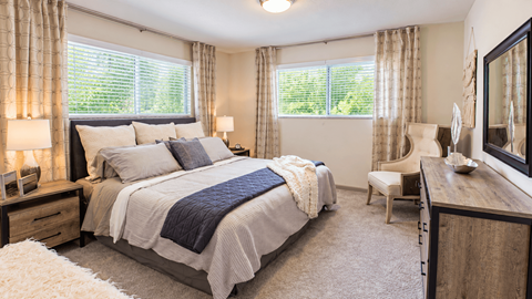 Furnished bedroom with two windows, bedside lamps, a dresser and an accent chair at Icon Avondale Apartments in Decatur, GA.