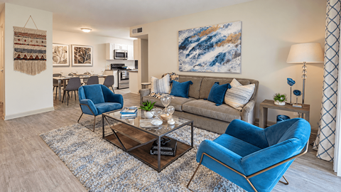 Furnished living room with a sofa and blue accent chairs, opening to the dining area and kitchen at Icon Avondale Apartments in Decatur, GA.