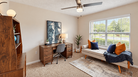 Furnished room with a desk, bookcase, and upholstered daybed beside a large window at Icon Cartersville.