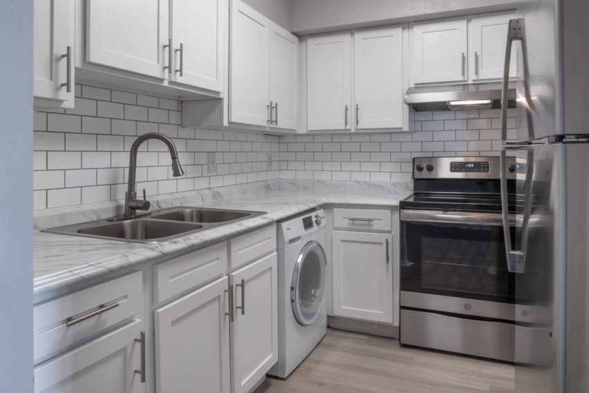 upgraded kitchen with white subway tile backsplash, white cabinets and brushed nickel hardware with gooseneck faucet.  Euro washer and dryer, and stainless steel stove and refrigerator. - Photo Gallery 1