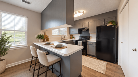 Apartment kitchen with gray cabinetry, breakfast peninsula, black appliances, and wood-style flooring at Madison Park in Birmingham, AL.