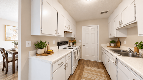 Galley-style apartment kitchen with white cabinets, double sink, and wood-style flooring at Madison Park Apartments & Townhomes.