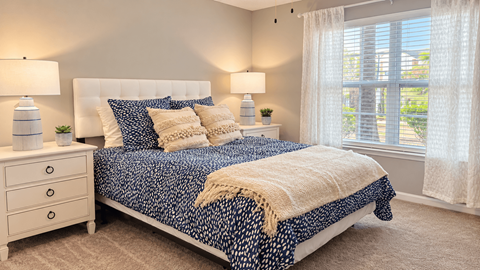 Furnished bedroom with upholstered headboard, navy patterned bedding and matching bedside lamps at Seaside Grove Apartments in Myrtle Beach, SC.