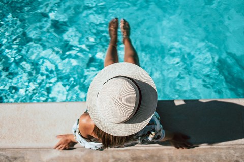 A woman in a hat is relaxing by the pool.