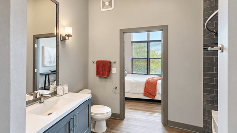 Bathroom with a white vanity countertop, gray cabinetry and a doorway to the bedroom at VER at Proscenium in Carmel, IN.