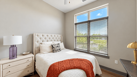 Apartment bedroom with a tufted headboard, bedside dresser and large window at VER at Proscenium in Carmel, IN.