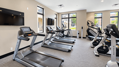 Fitness center with treadmills, elliptical machines and exercise bikes beside large windows at VER at Proscenium in Carmel, IN.