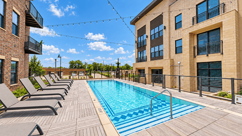 Outdoor swimming pool with entry steps and chaise lounges between apartment buildings at VER at Proscenium in Carmel, IN.