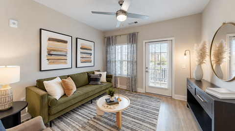 Apartment living room with green sofa, coffee table and glass balcony door at The View on Canton in Cartersville, GA.