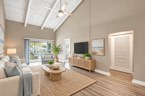 Virtually staged living room with a vaulted ceiling, exposed beams and sliding balcony doors at Waterchase Apartments in Largo, FL.
