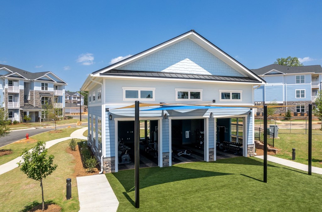 outdoor green yoga lawn just outside the fitness center with garage doors rolling up.  The lawn is partially covered and shaded.