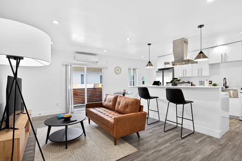 A modern living room with a brown leather sofa and a white kitchen in the background.