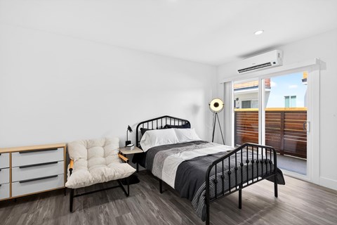 A bedroom with a black metal bed and a white chair with a wooden frame.