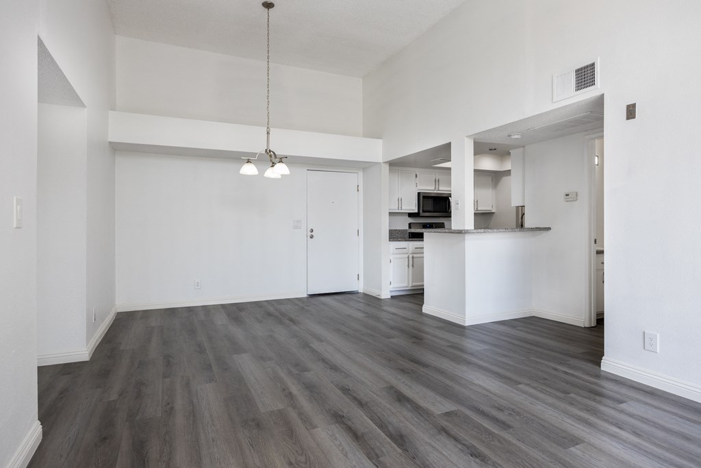 an empty living room and kitchen with white walls and wood flooring
