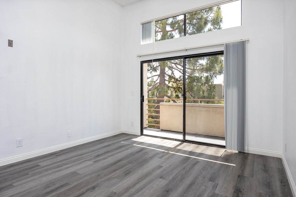 an empty living room with a sliding glass door to a balcony