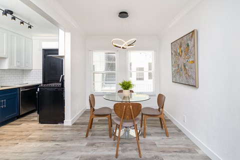 a dining room with a glass table and chairs and a kitchen with a black refrigerator