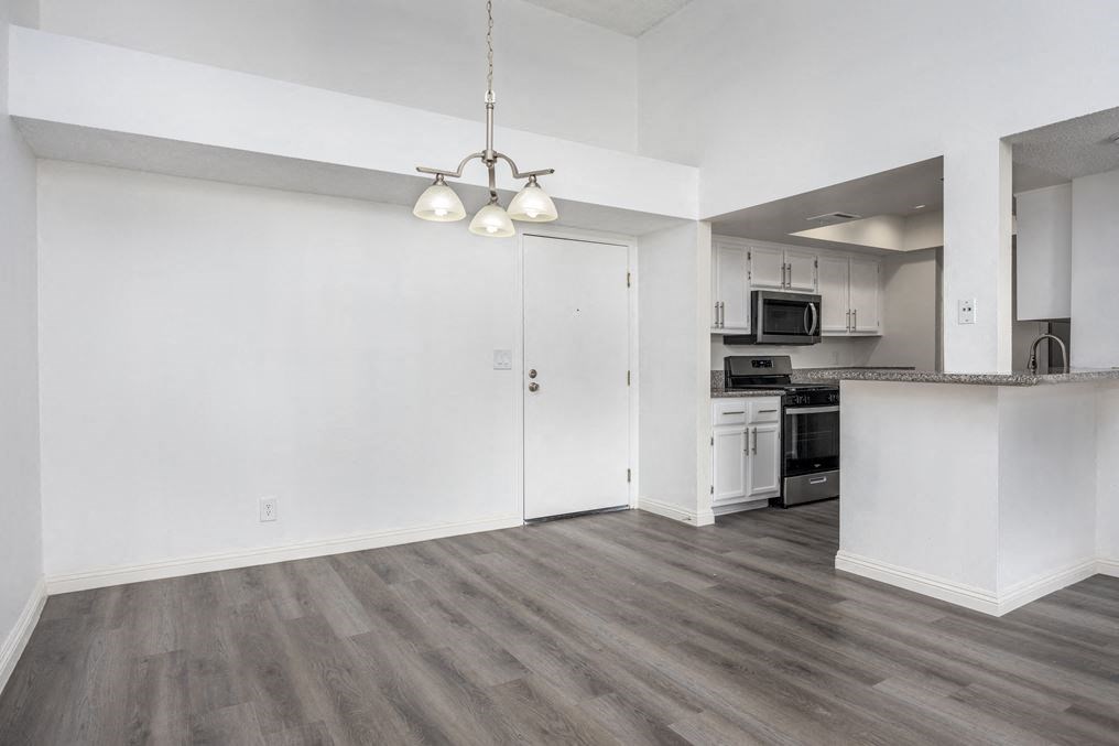 an empty living room with a kitchen in the background