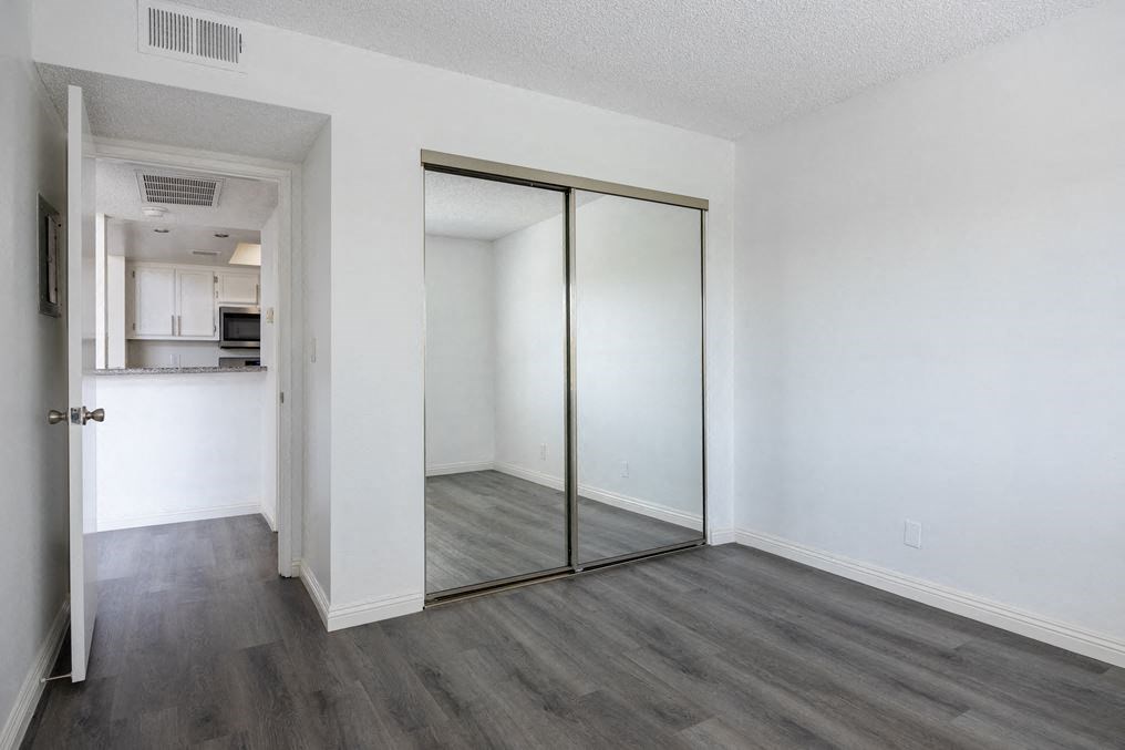 a bedroom with a mirror and a kitchen in the background