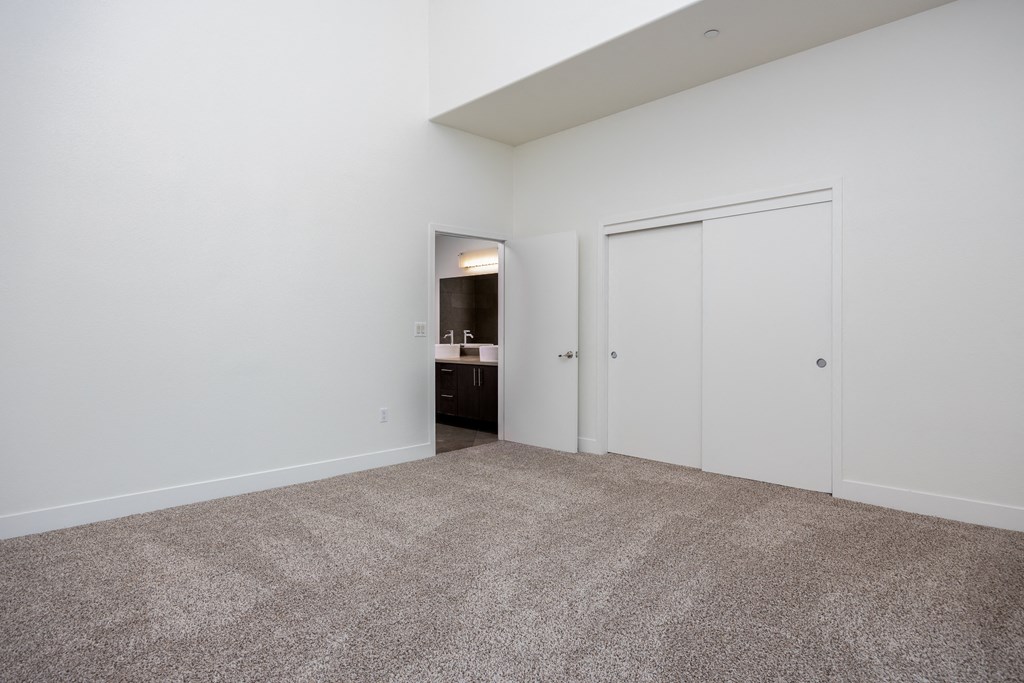 a bedroom with white walls and carpet and doors to a bathroom