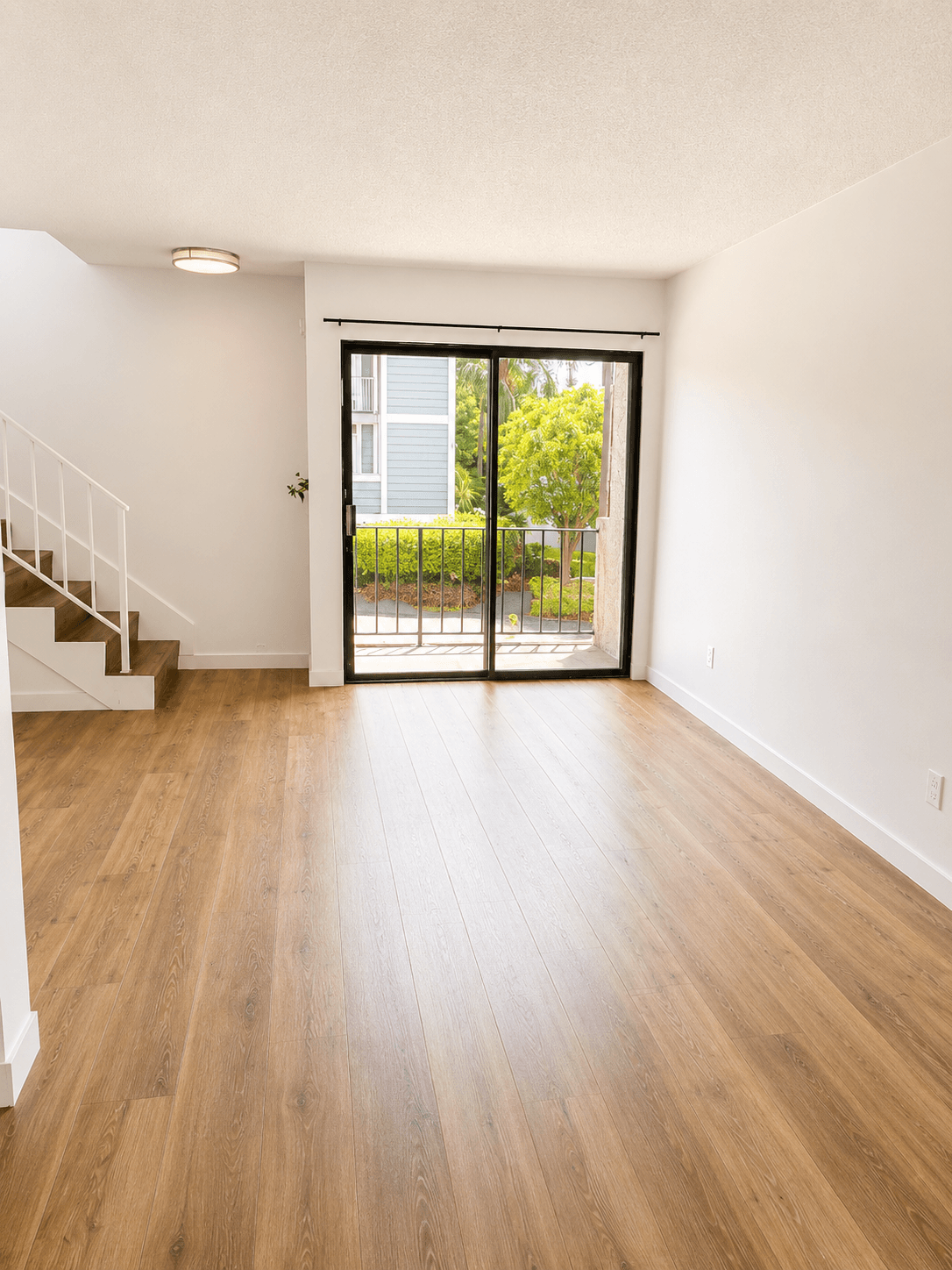 A room with a wooden floor and a staircase on the left side.