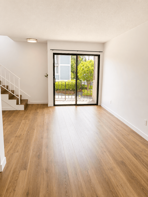 A room with a wooden floor and a staircase on the left side.