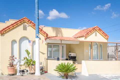 A yellow house with a red roof and a palm tree in front.