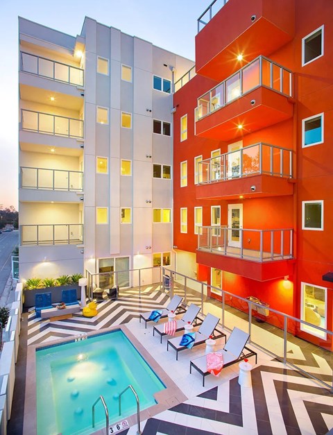 A swimming pool is surrounded by lounge chairs in a courtyard.