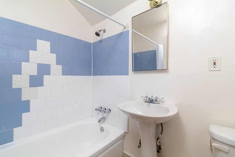 A white pedestal sink sits under a mirror in a blue tiled bathroom.