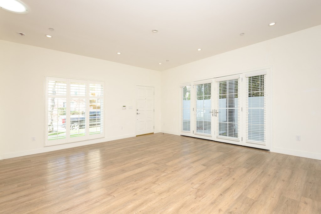 a living room with white walls and wood flooring and windows