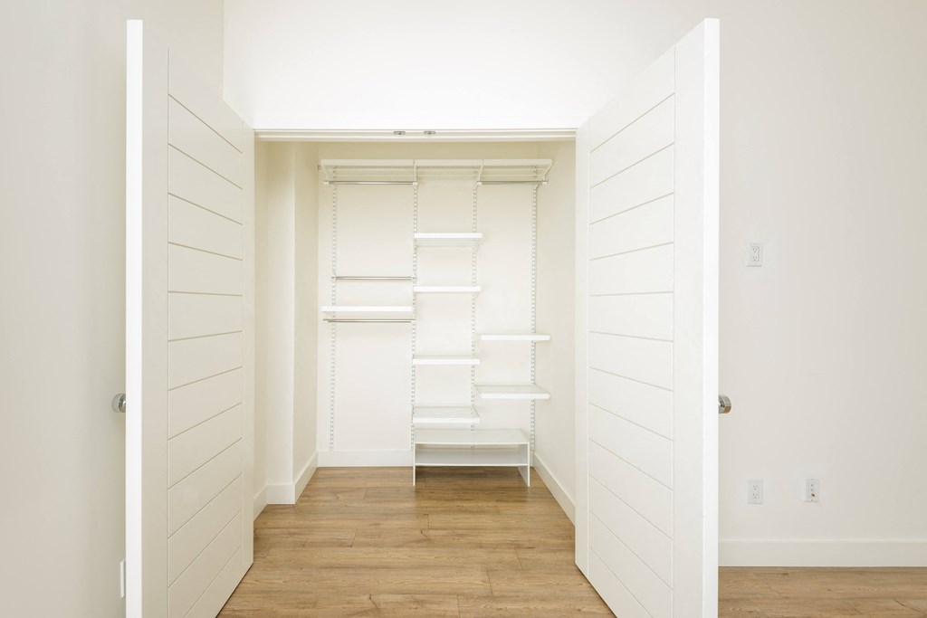 a large white closet with shelves and a staircase in a room with wood floors