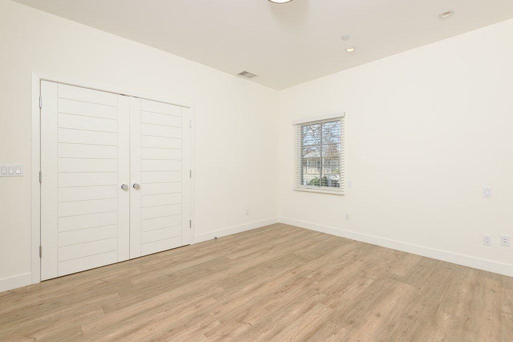 a bedroom with white walls and wood floors and a closet