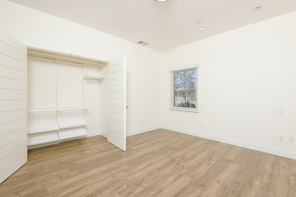 a bedroom with white walls and wood floors and a closet